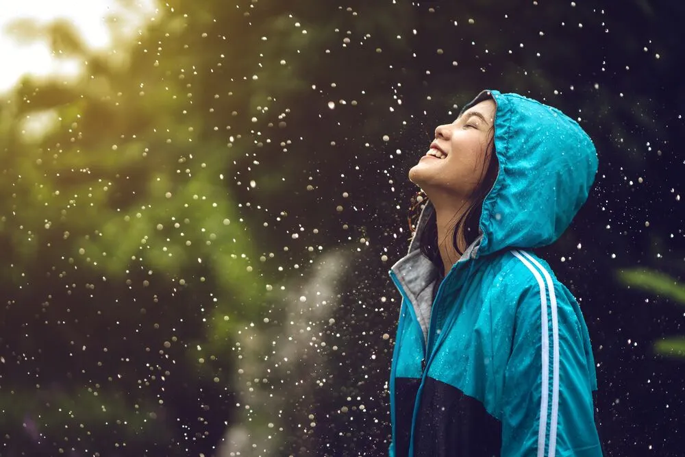 Asian lady on a blue green coat on a rainy day with trees on background